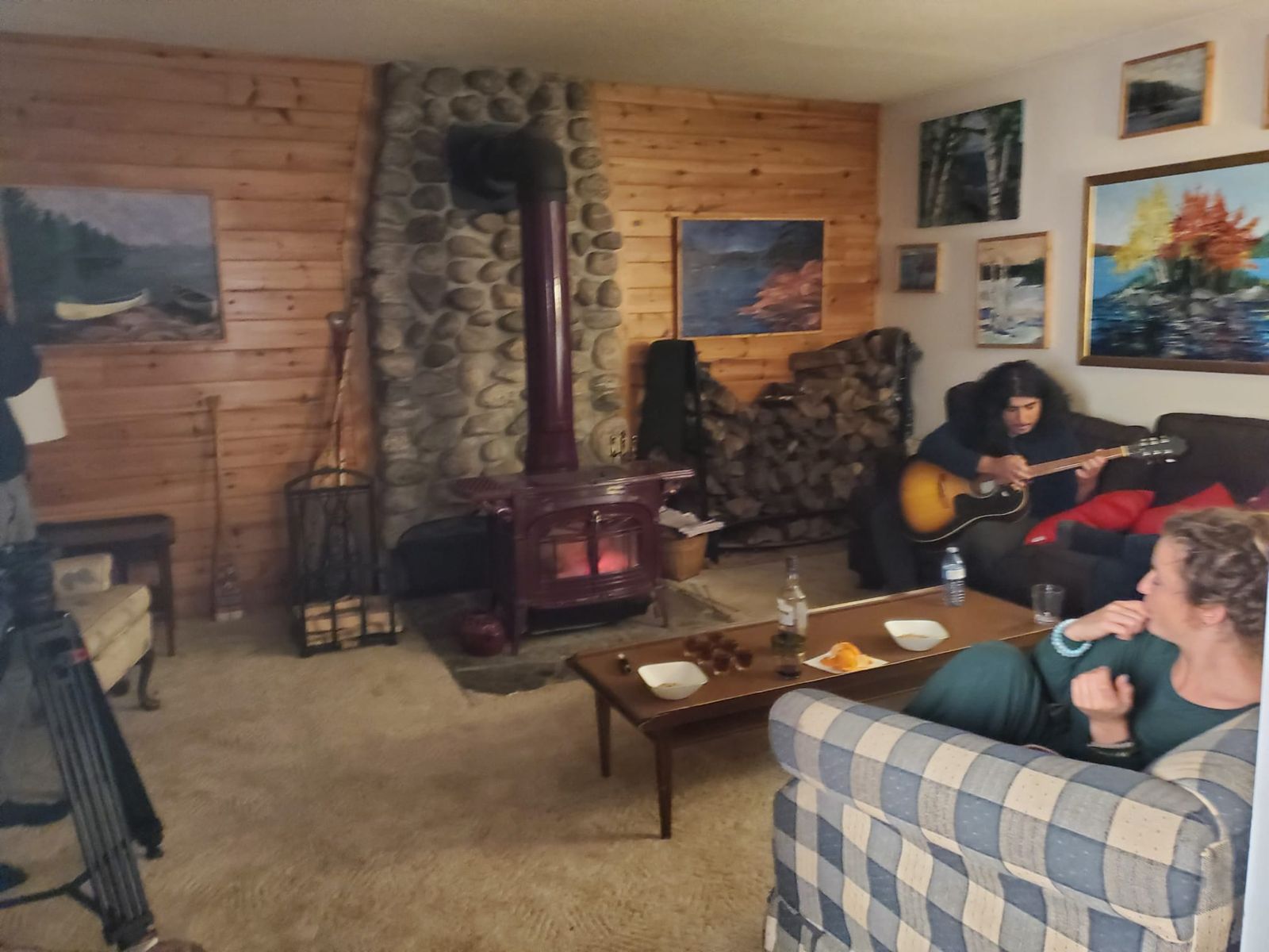Living room set with a guitar player by the wood stove and an actor on the couch