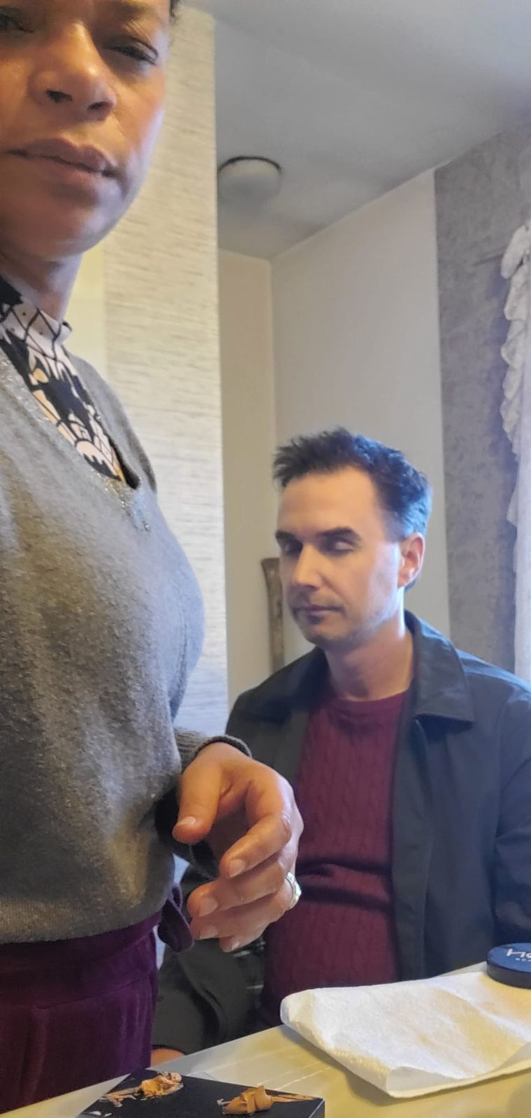 Jason Carson in a maroon sweater and grey jacket, eyes closed while getting his makeup done