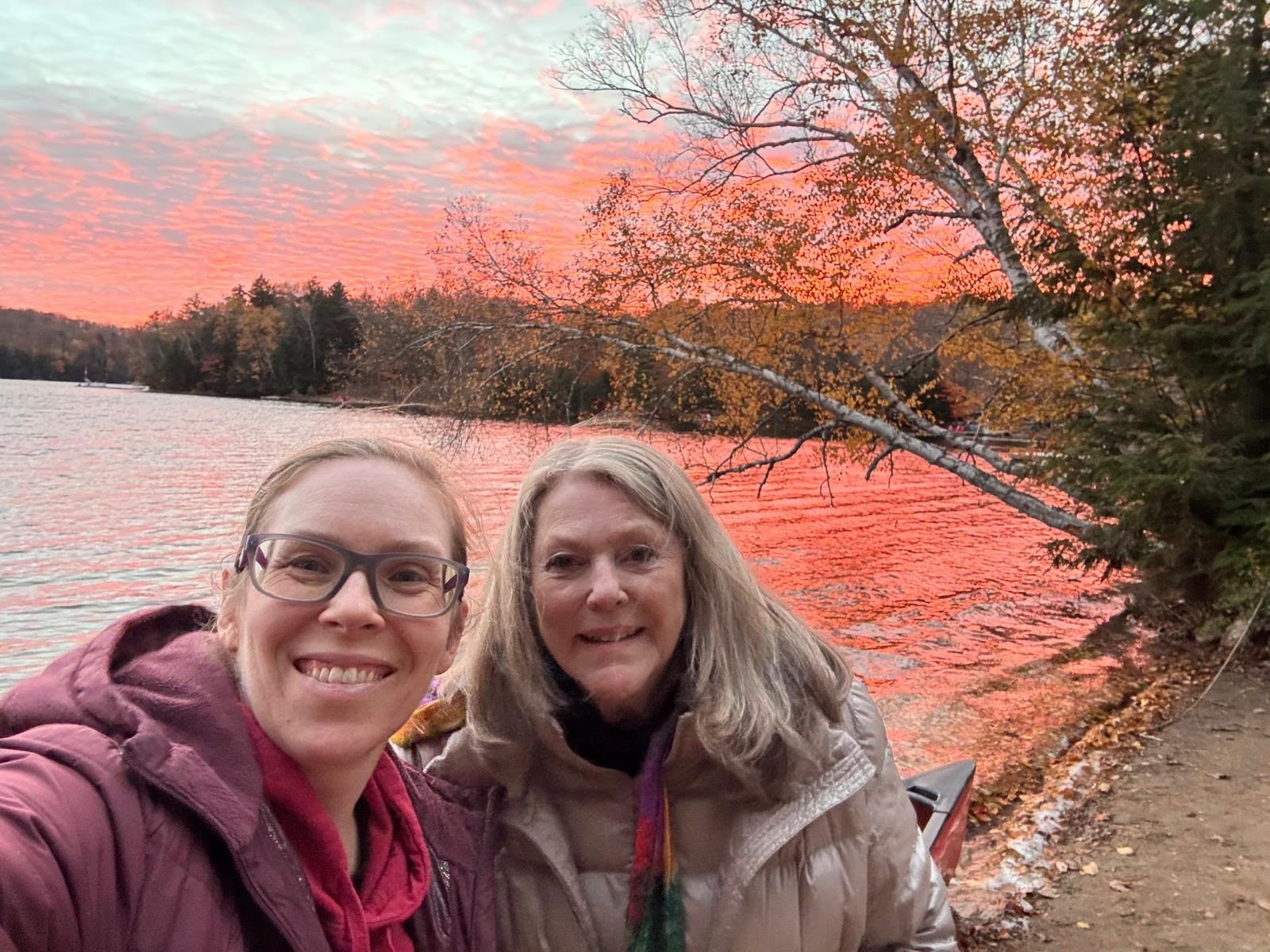 Two crew members smiling by the lake under a bright pink sunset