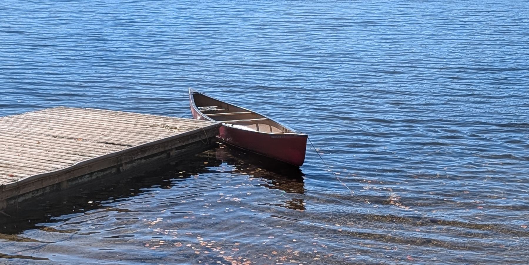 A red canoe tied to a weathered wooden dock on dark water