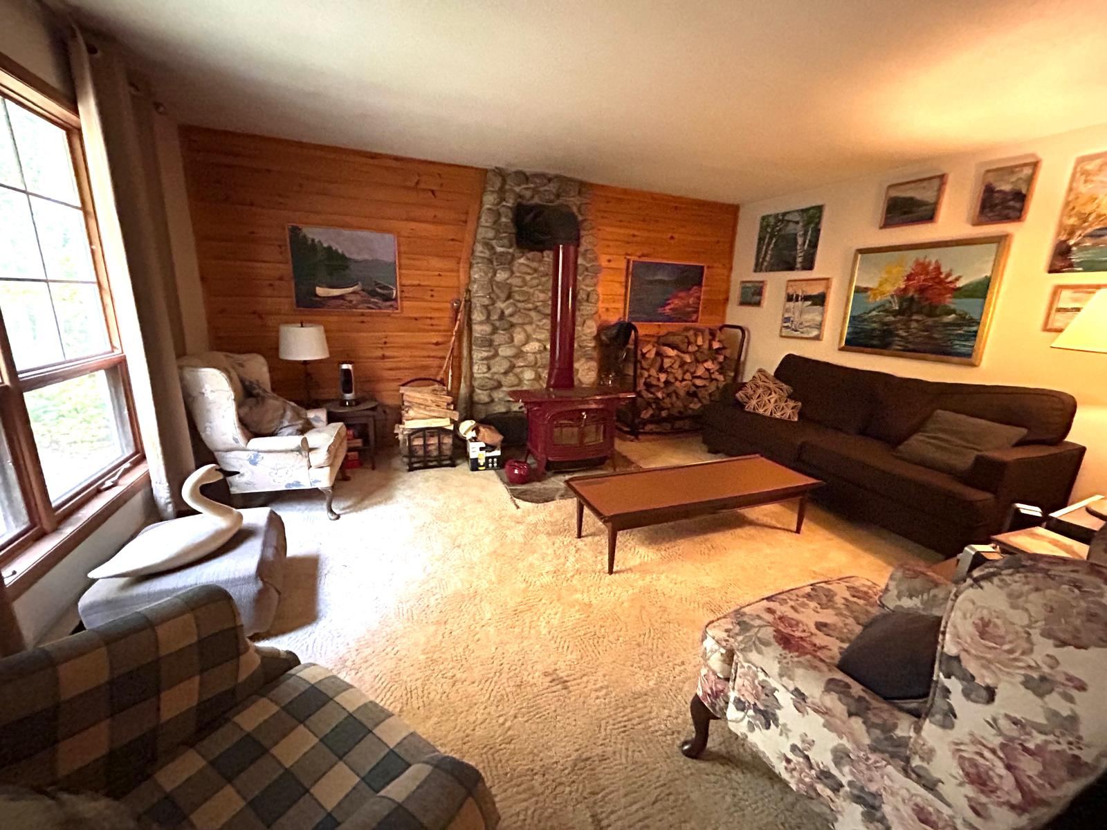A wood-panelled living room with a red stove against a stone chimney