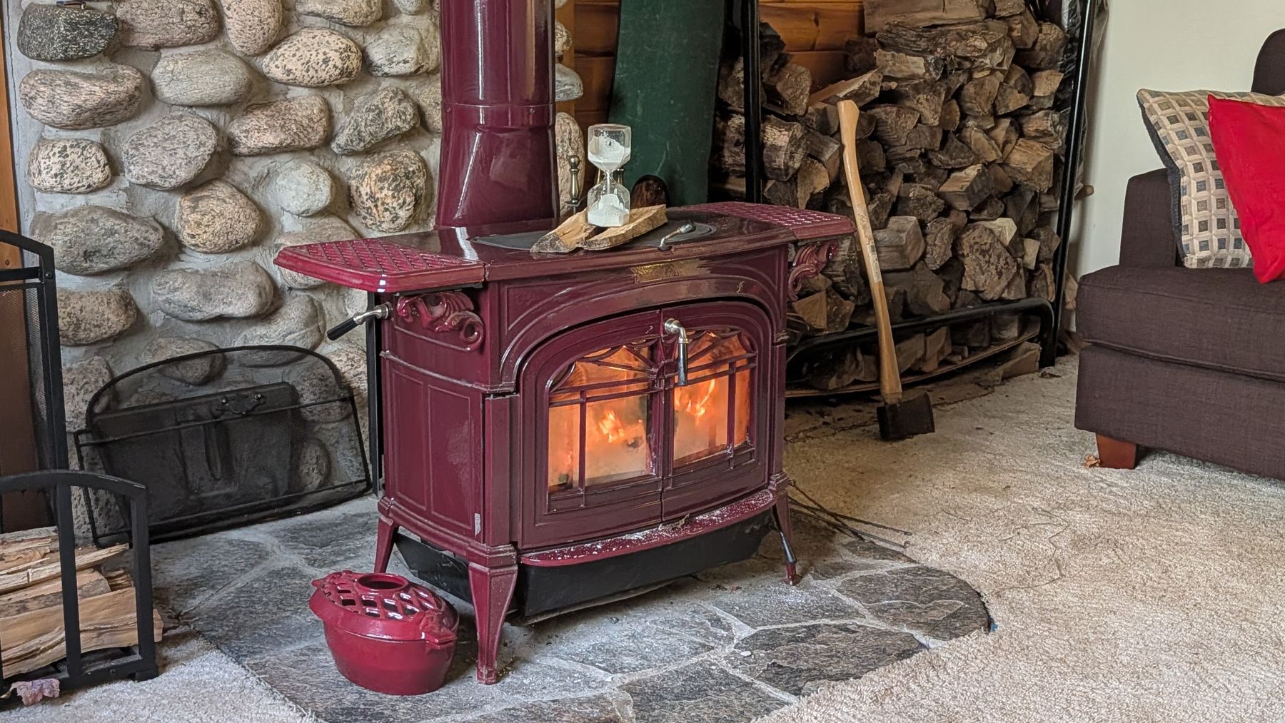 An antique hourglass on top of a red cast-iron wood stove
